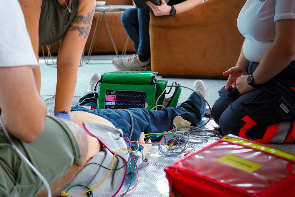 Fortbildungs-Trio, Teil 1: ACLS Provider – Reanimationsteam am Boden, Monitor zeigt Rhythmus und Vitalwerte